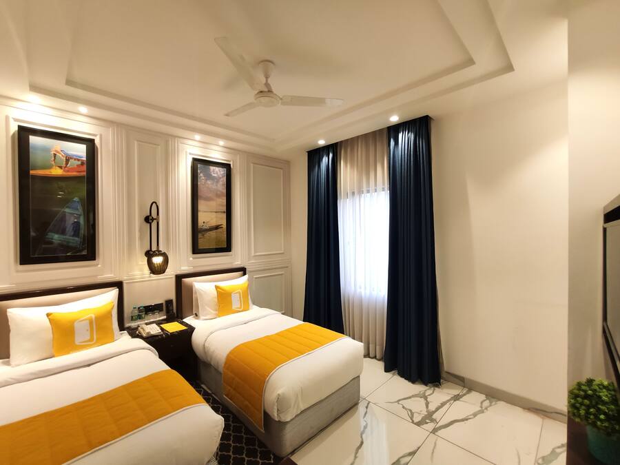 A hotel room with two beds, a ceiling fan, framed artwork, a nightstand, a TV, and a window with curtains.
