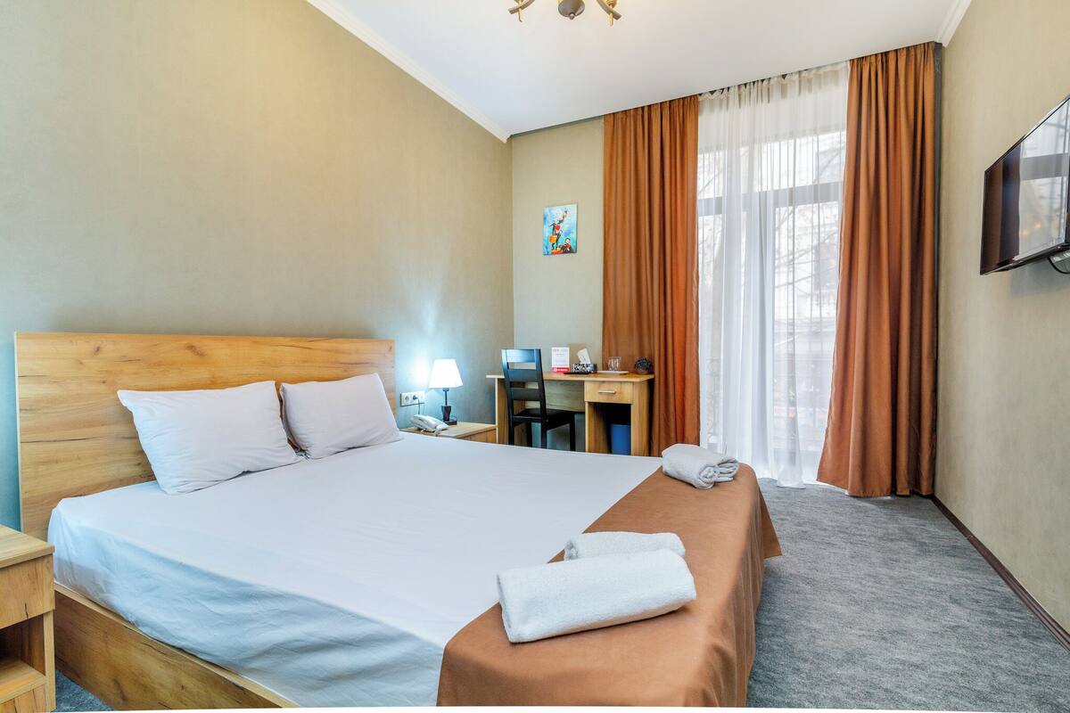 A hotel room with a large bed, a desk, a chair, a TV, and a painting on the wall.
