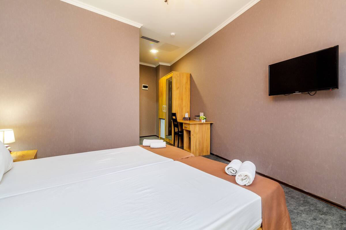 A hotel room with a bed, a desk, a chair, a TV, and a bathroom visible through an open door.