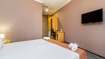 Habitación de hotel con cama, escritorio, silla, televisor y baño visible a través de una puerta abierta.