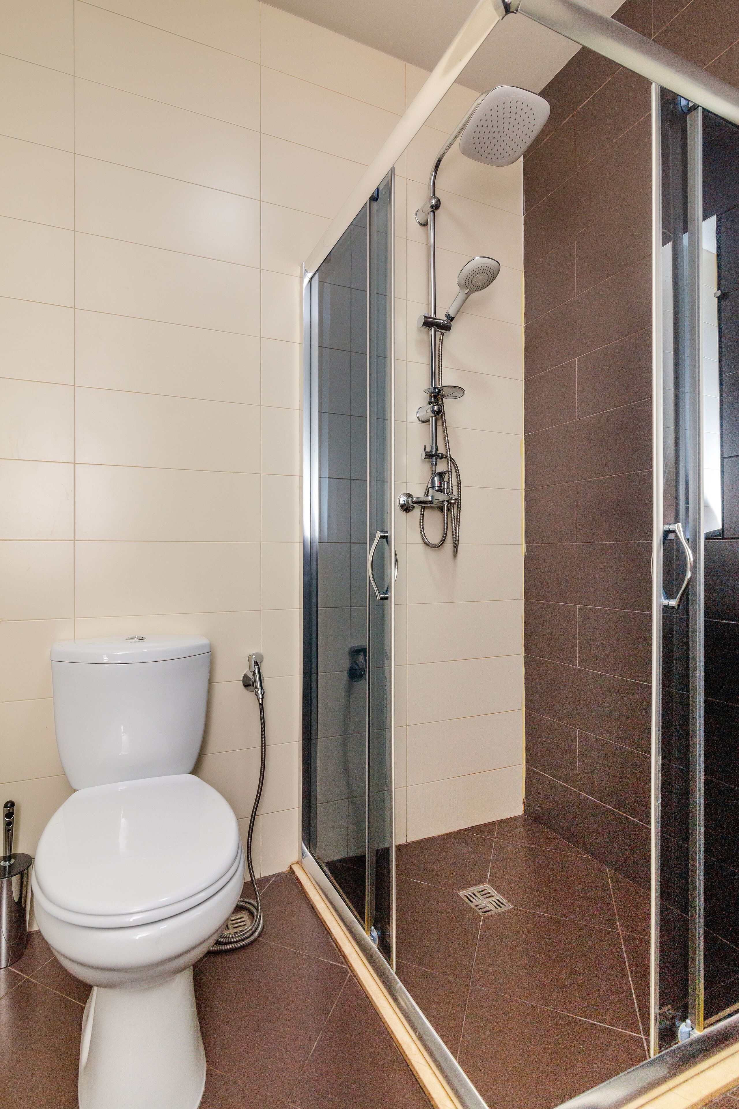 A bathroom with a toilet, a shower with a glass door, and brown tiles.