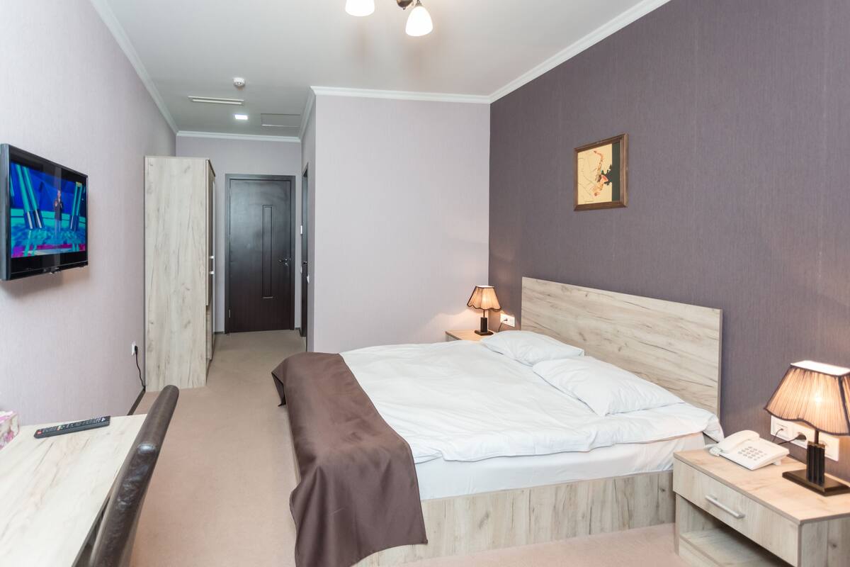 A hotel room with a bed, bedside lamps, a TV, and a wooden headboard.