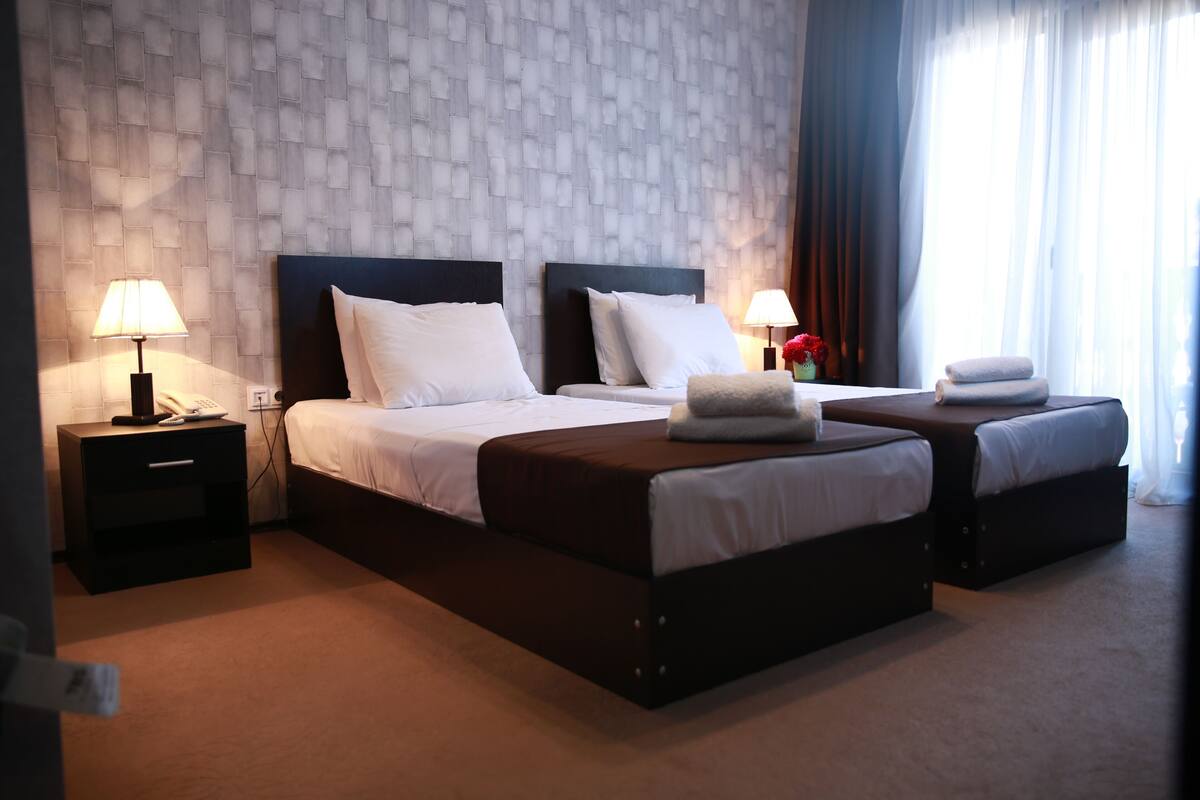 A hotel room with a large bed, two bedside tables with lamps, and a window with curtains.