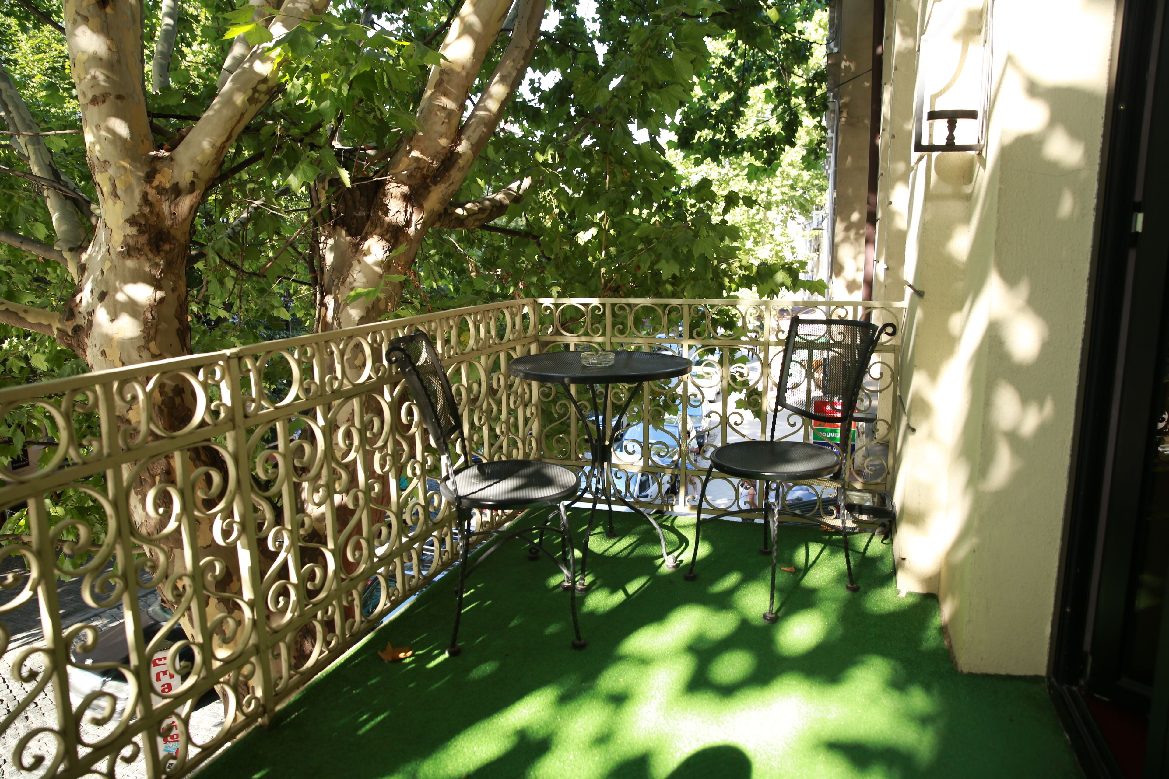 A balcony with a wrought iron railing, two chairs, and a small table.