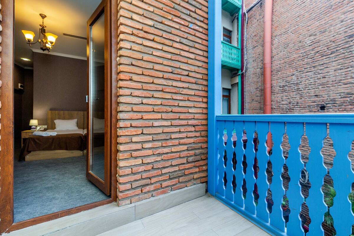 A hotel room with a brick wall, a wooden door, and a blue balcony railing.
