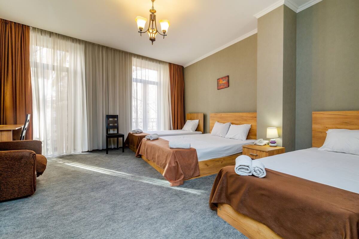 A hotel room with three beds, a desk, a chair, and a chandelier.