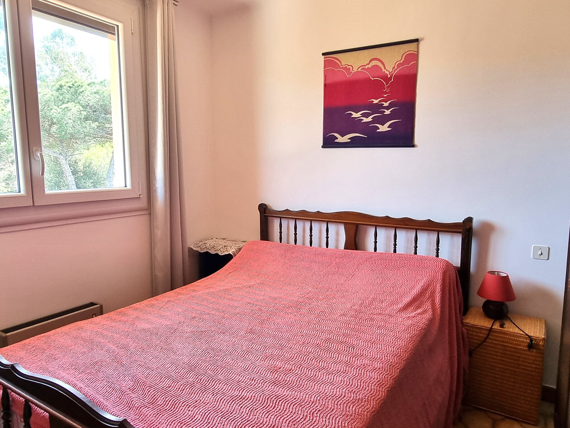 A bedroom with a bed, a window, a nightstand, a lamp, and a wall hanging.