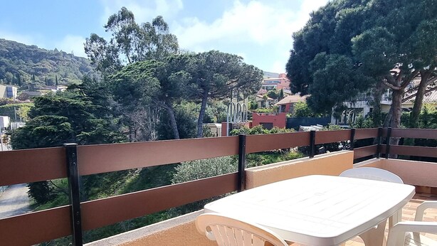 A balcony with a white table and chairs, overlooking a hilly landscape with trees and buildings. - Port-Vendres: T2 with terrace and parking (Port-Vendres)