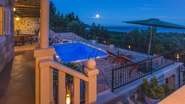 Una piscina de piedra con vista al mar, un área de estar cubierta y una escalera de piedra.