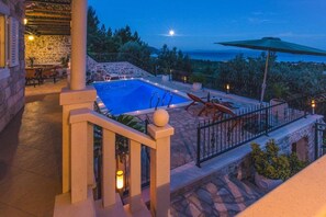 Una piscina de piedra con vista al mar, un área de estar cubierta y una escalera de piedra.