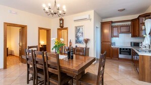 Un comedor con una mesa y sillas de madera, un candelabro, y una cocina con muebles y electrodomésticos de madera.