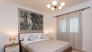 Un dormitorio con una cama, mesitas de noche, un cuadro y una ventana con cortinas.