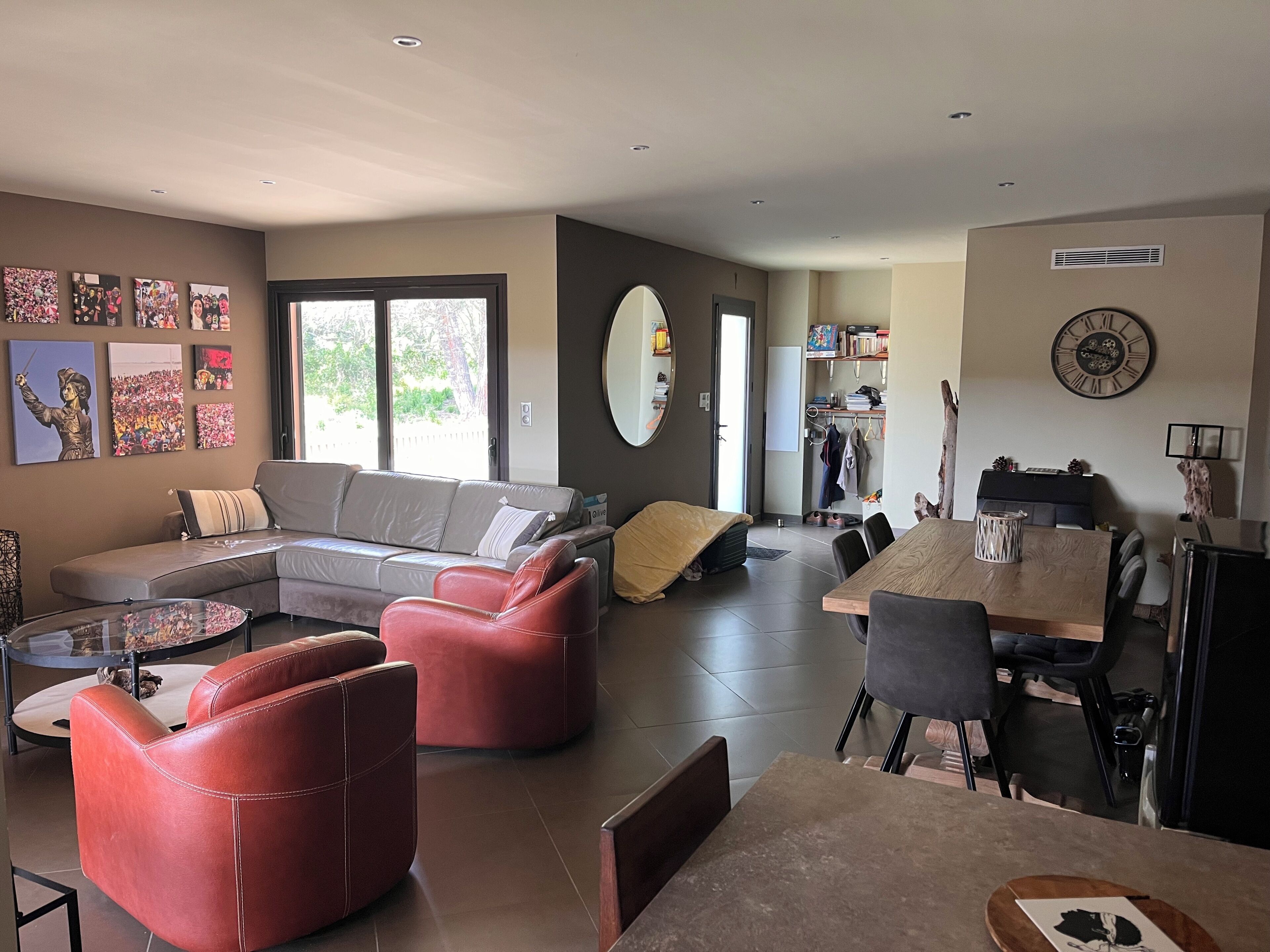A modern living room with a sectional sofa, red chairs, a dining table, and a large mirror.
