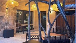 A dining area with a stone wall, wooden furniture, and hanging lights. - Villa Apartment T4 with 4 terraces Porto Vecch swimming pool garden quiet (Porto-Vecchio)