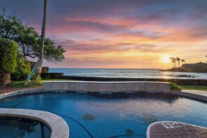 Una piscina con vistas al océano y al atardecer, rodeada de vegetación y palmeras.