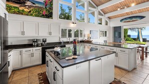 Una cocina amplia con una isla grande, muebles blancos y vistas al océano.