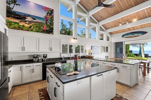 Una cocina amplia con una isla grande, muebles blancos y vistas al océano.