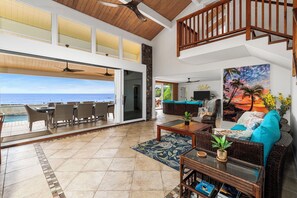 Amplia sala de estar con vista al océano, comedor con asientos al aire libre y una zona de estar acogedora con un cuadro.