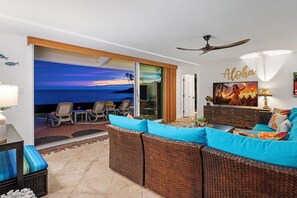 Un salon avec vue sur l’océan, des meubles en osier et un ventilateur de plafond.