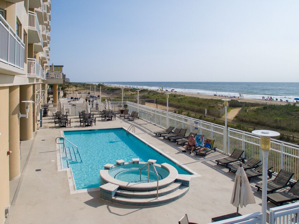 A pool area with lounge chairs and a view of the beach.