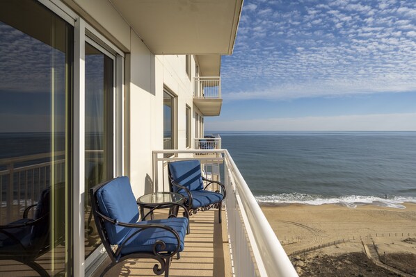 Un balcón con dos sillas azules y una mesa de vidrio con vista a una playa.