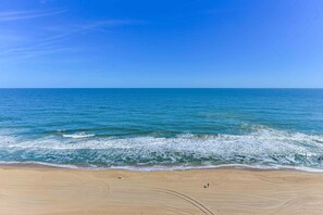 A beach with a clear view of the ocean, sandy shore, and a few people walking.