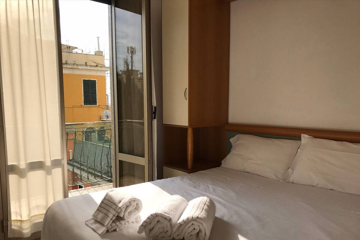 A hotel room with a bed, a wooden headboard, and a view of a balcony with a chair and a table.