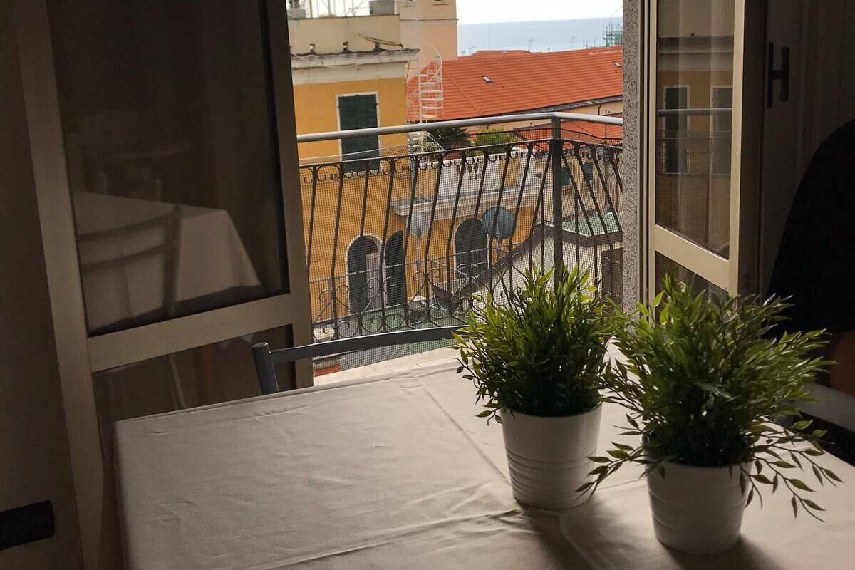 A balcony with a table and two potted plants, overlooking a cityscape with buildings and a tower.