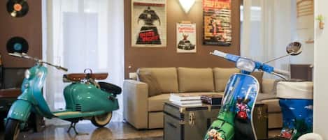 Una habitación con dos scooters antiguos, un sofá y una pequeña mesa con libros y un objeto decorativo.