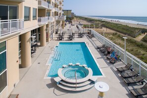 A rooftop pool with a circular hot tub, lounge chairs, and a view of the beach.