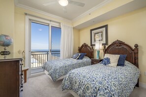 A bedroom with two beds, a globe, and a view of the ocean through a sliding door.