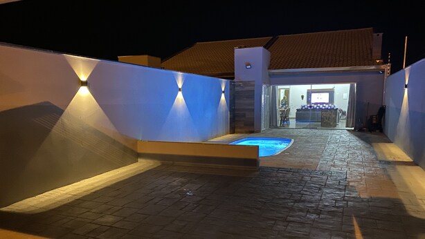 A nighttime view of a swimming pool area with a stone floor and walls, and a building entrance in the background. - FAMILY HOUSE-Olympia  (Olímpia)