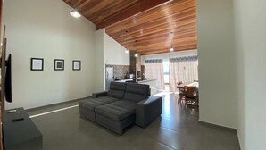A modern living room with a sectional sofa, a flat-screen TV, and a dining area with a table and chairs. - FAMILY HOUSE-Olympia  (Olímpia)