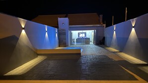 A nighttime view of a building's entrance with illuminated walls and a tiled pathway leading to a door. - FAMILY HOUSE-Olympia  (Olímpia)