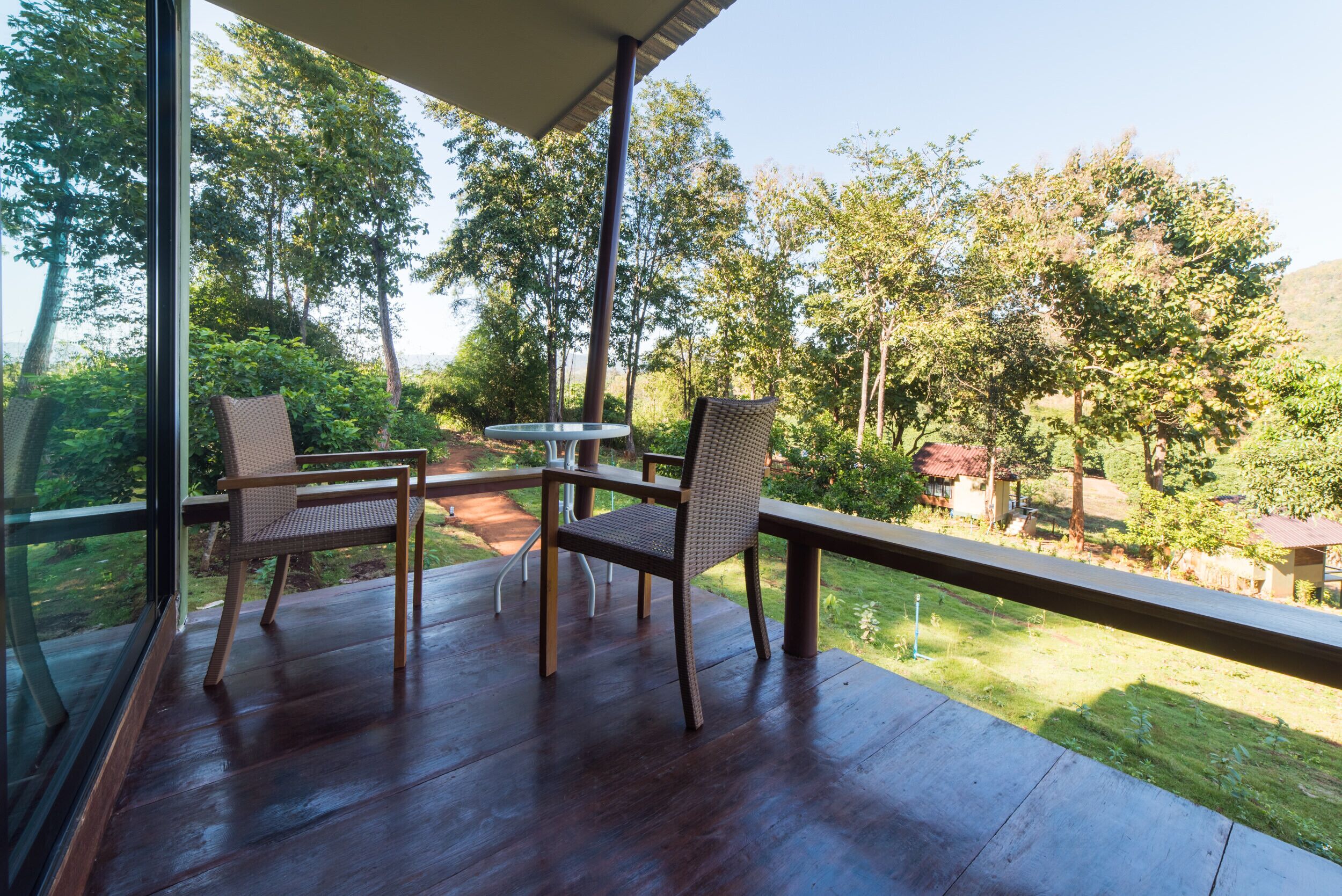 An outdoor deck with two wicker chairs and a small table, overlooking a lush garden and distant buildings.