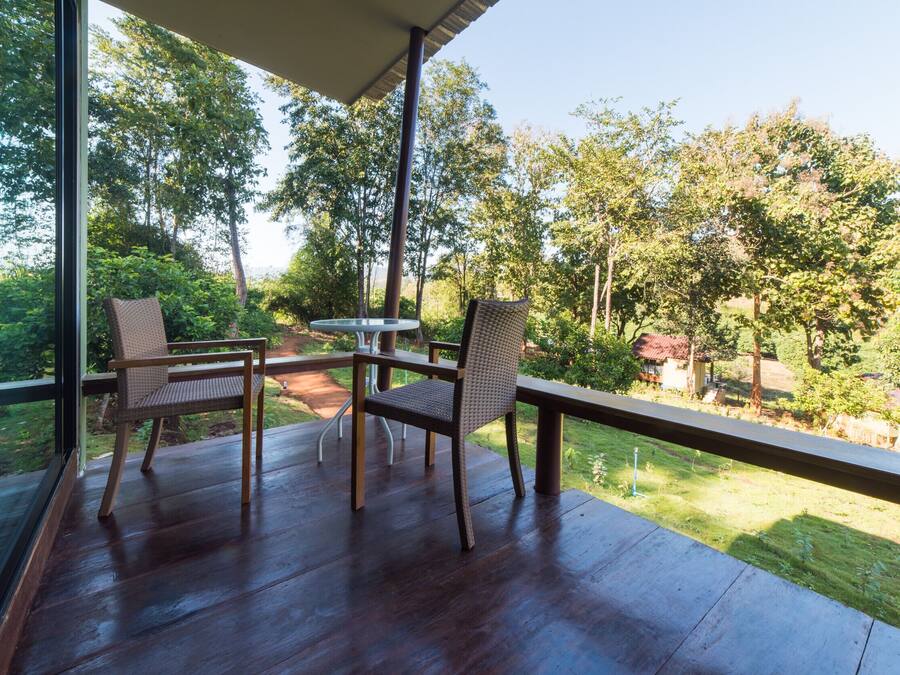 An outdoor deck with two wicker chairs and a small table, overlooking a lush garden and distant buildings.