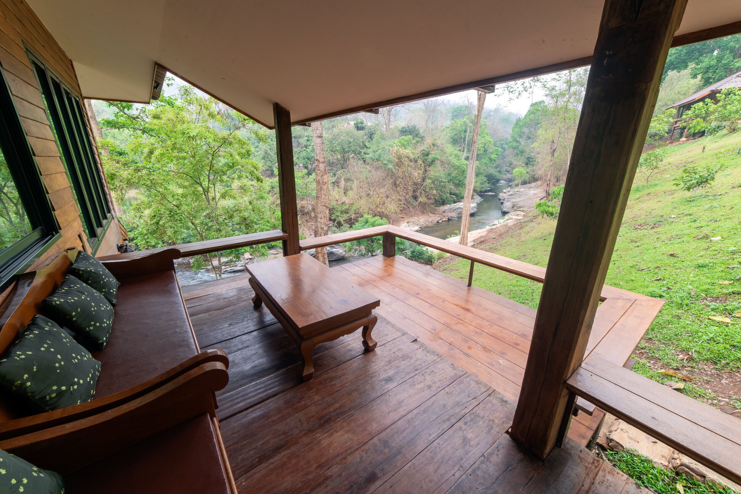 A wooden deck with a bench and a table, overlooking a lush green landscape and a river.