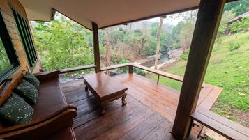 A wooden deck with a bench and a table, overlooking a lush green landscape and a river.