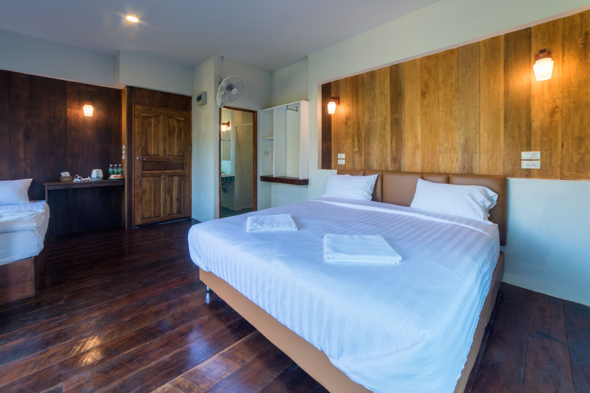A hotel room with a large bed, wooden panel walls, a wooden floor, and a small desk with toiletries.