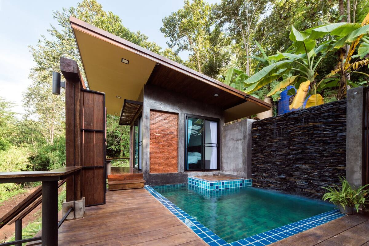 A modern house with a pool, wooden deck, and a stone wall.