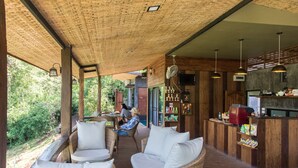 A covered outdoor seating area with wicker furniture and a bar with various items on shelves. - Chiang Mai Elephant Friends (Mae Wang)