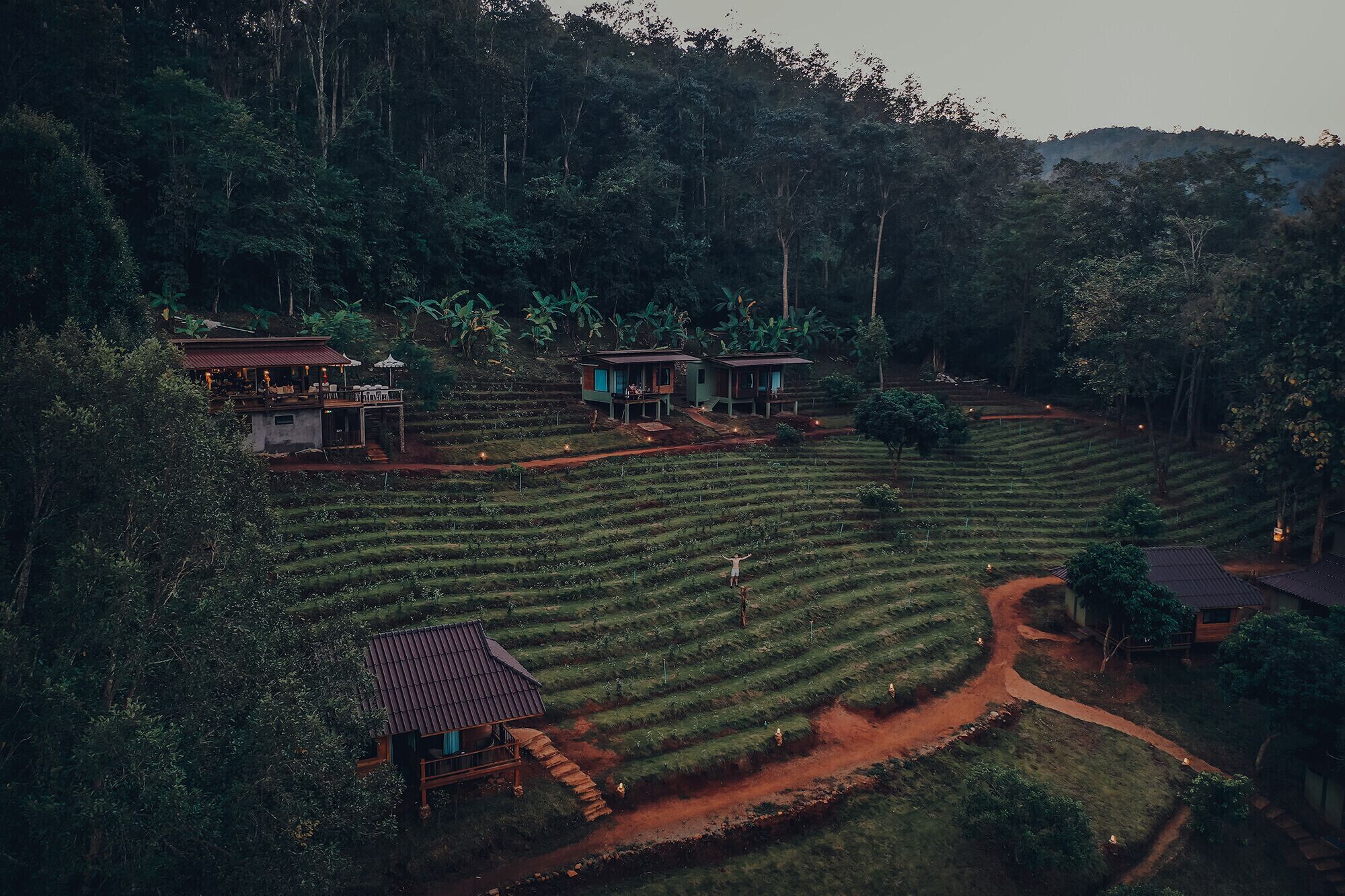 A terraced landscape with multiple wooden structures, likely accommodations, surrounded by dense forest.