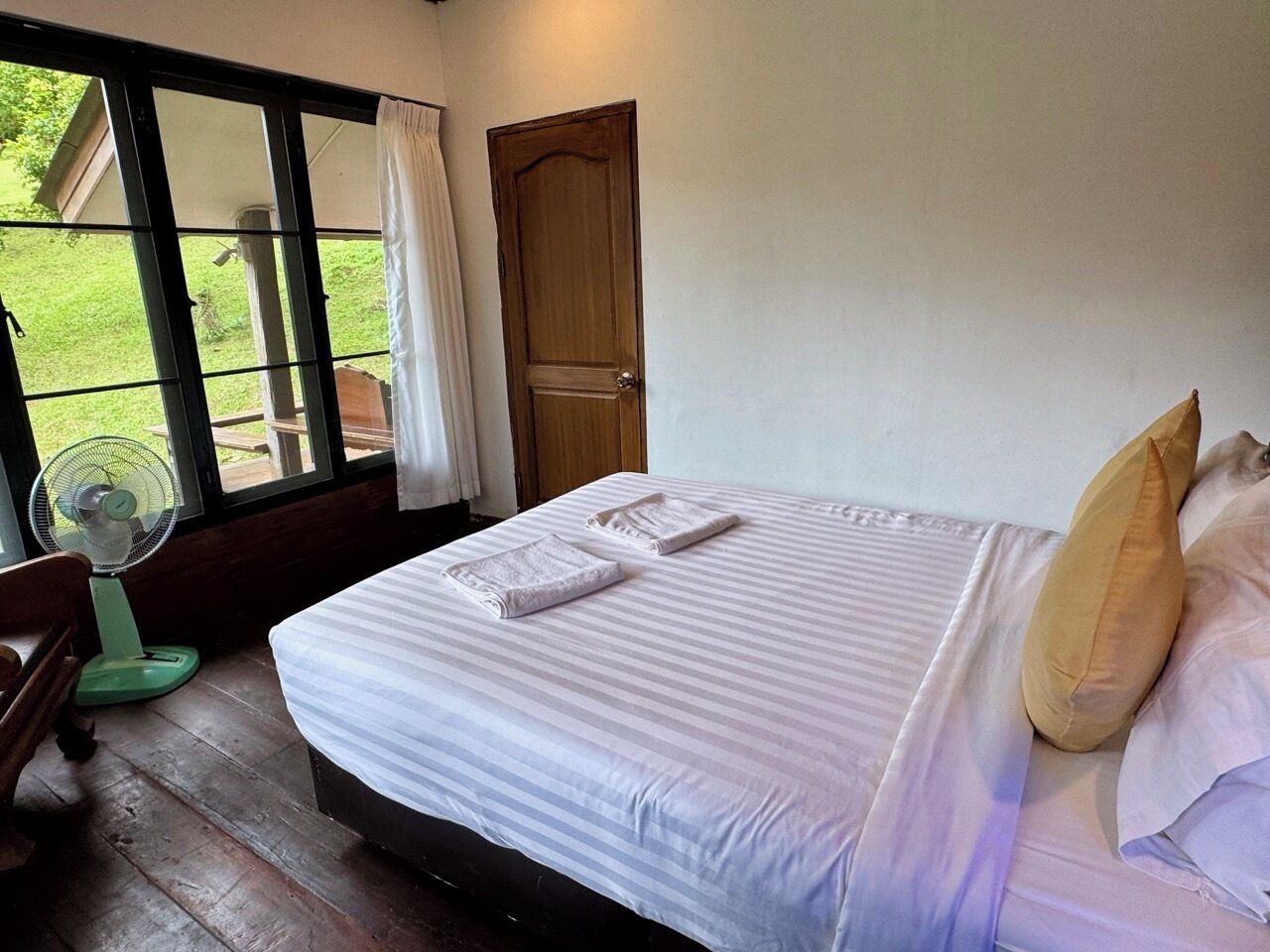 A bedroom with a bed, pillows, a fan, and a window with curtains.