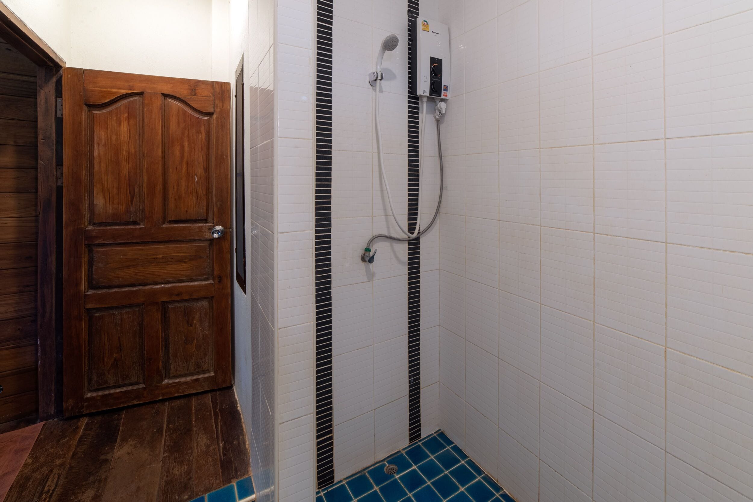 A bathroom with a wooden door, white tiled walls, and a blue-tiled floor.