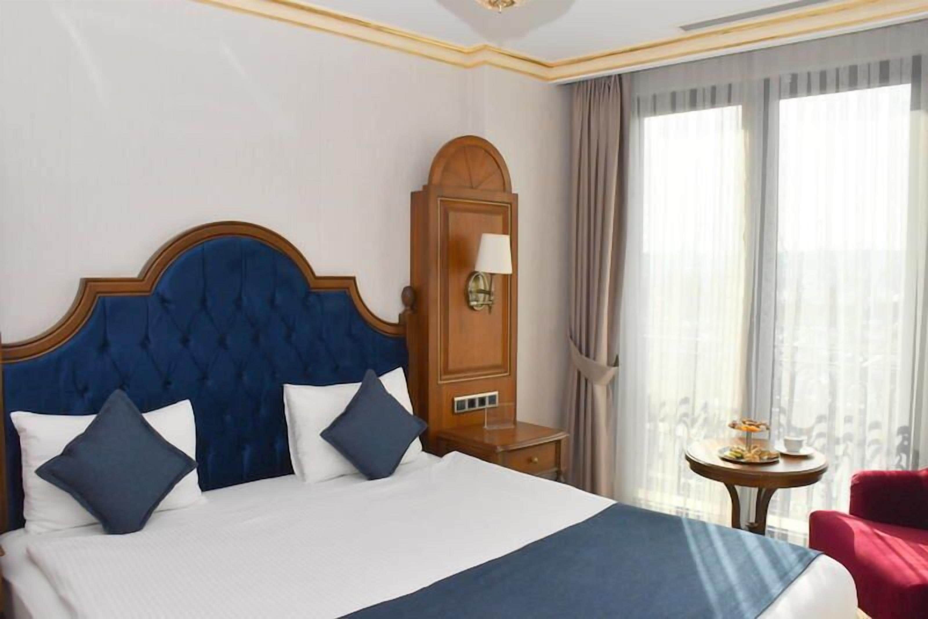 A hotel room with a large bed, a wooden nightstand, a red chair, and a window with curtains.