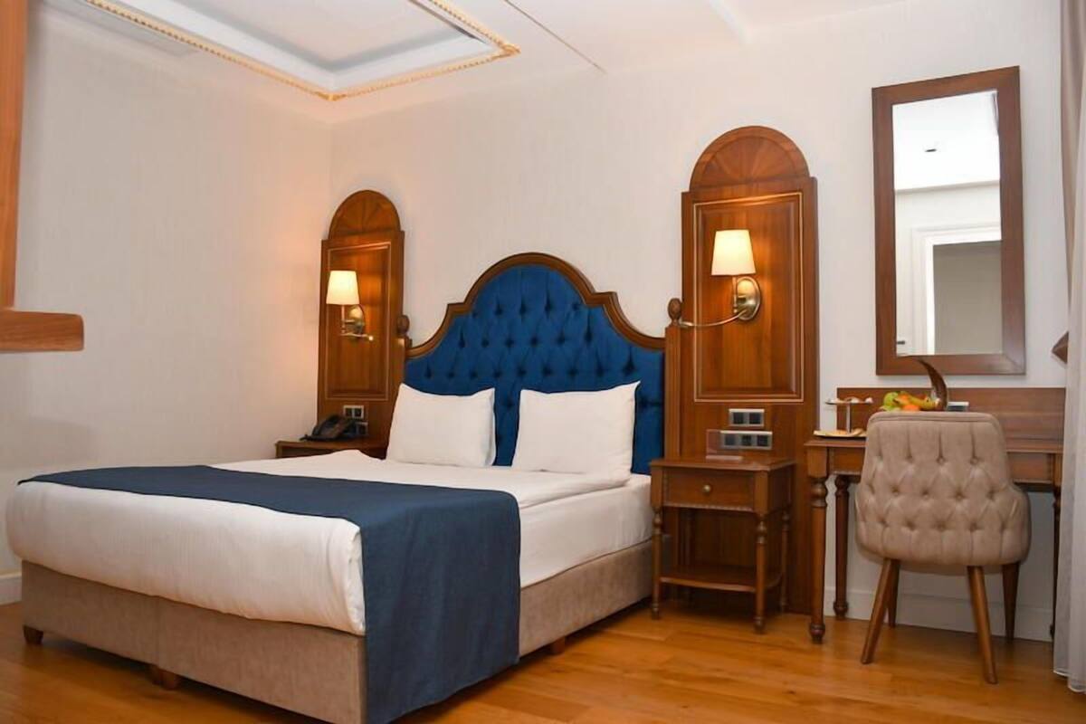 A hotel room with a large bed, wooden headboard, two bedside tables with lamps, a mirror, and a chair.