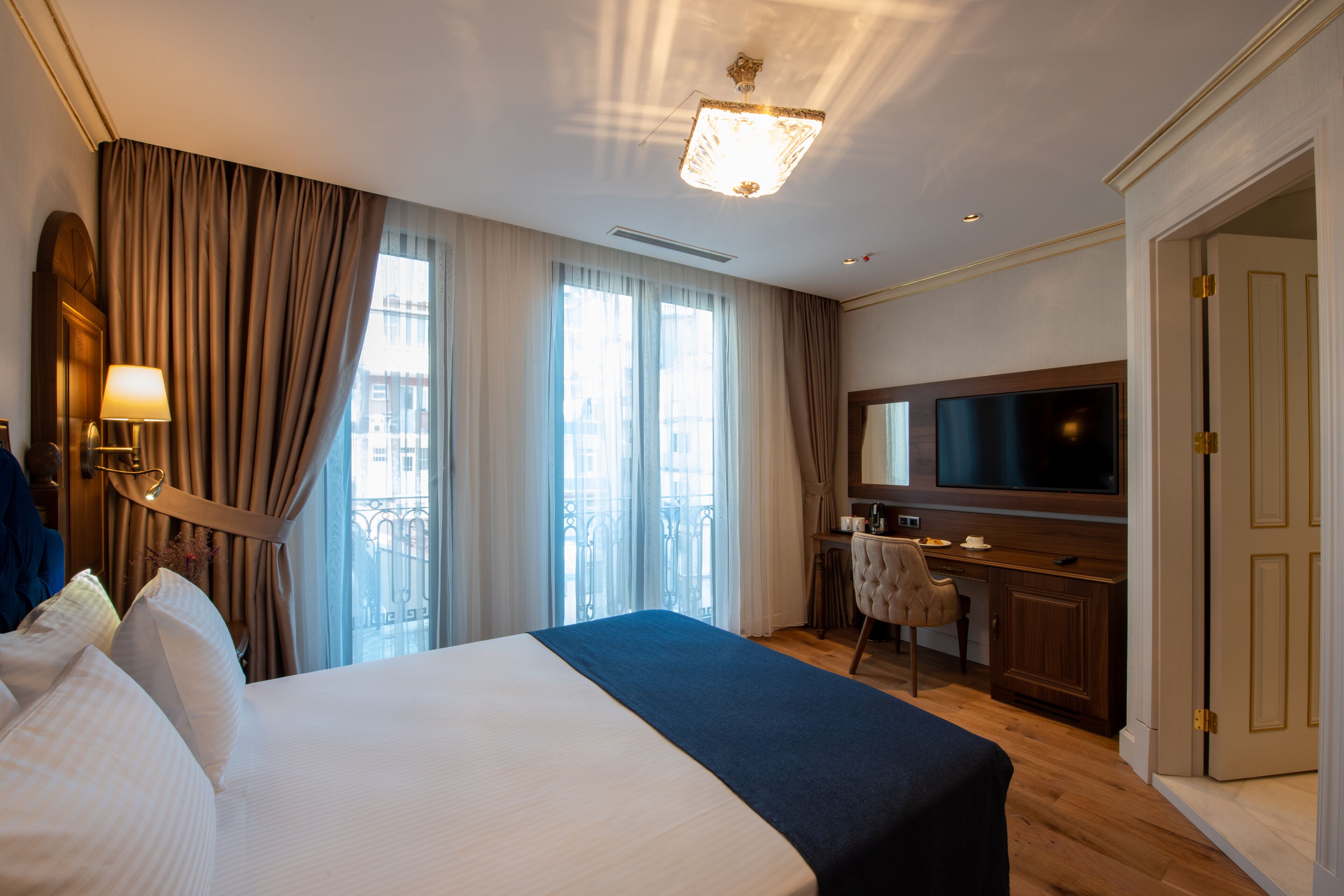 A hotel room with a large bed, a desk with a chair, a television, and a wardrobe.