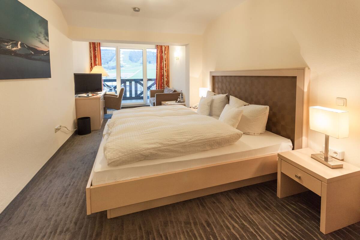 A hotel room with a large bed, a desk with a computer, a chair, and a view of a balcony.