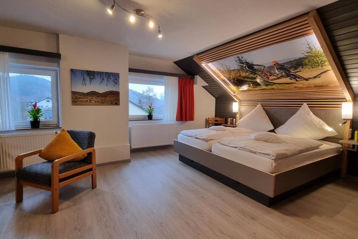 A modern bedroom with a sloped ceiling, a bed, a chair, and a window with curtains.
