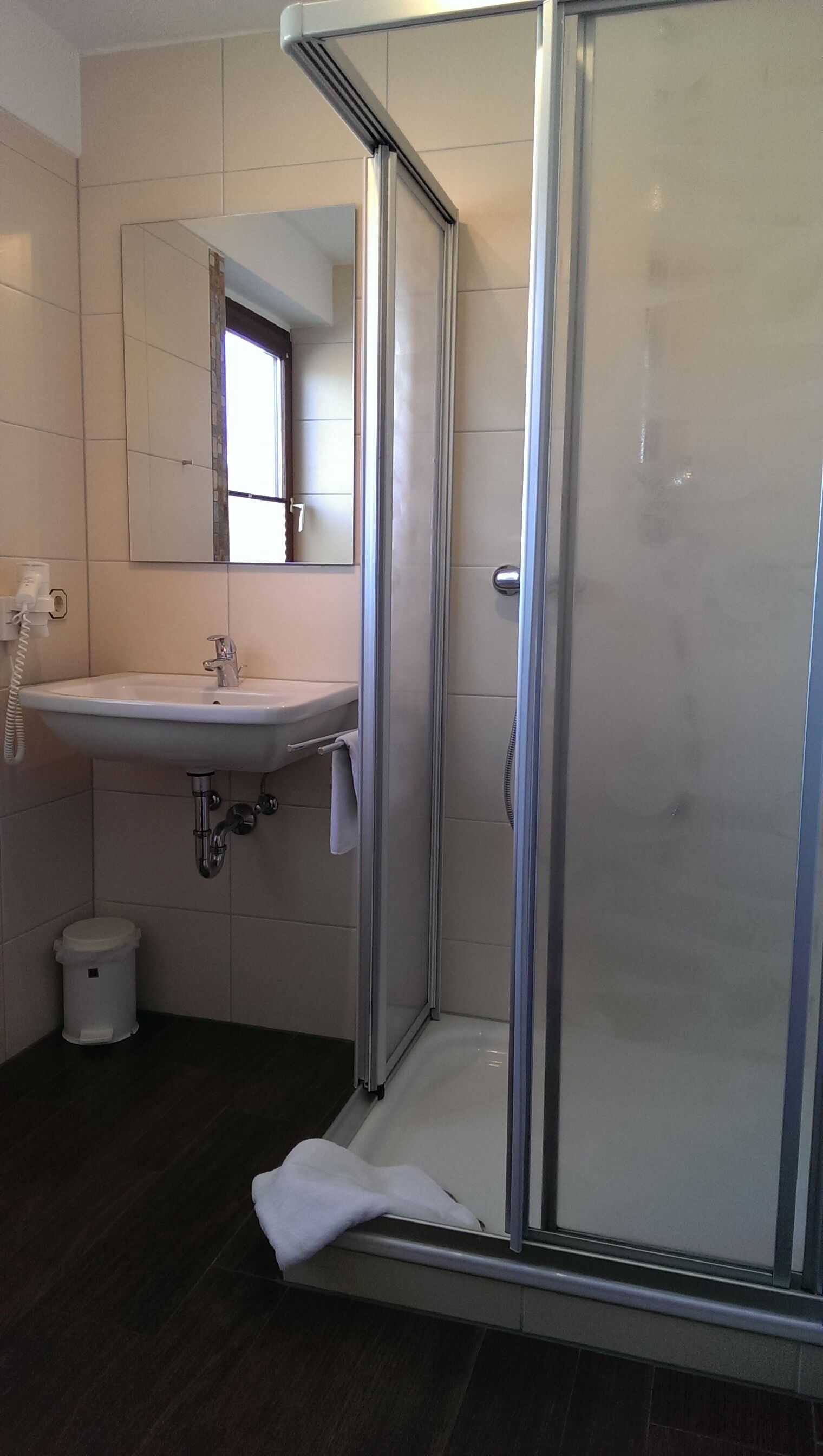 Ein Badezimmer mit einer Duschkabine, einem Waschbecken mit Spiegel darüber und einem Mülleimer.